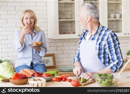 senior man cutting vegetables chopping board looking her wife eating muffins kitchen