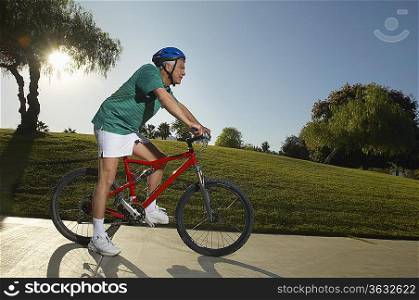Senior man cycling in park at dusk, side view
