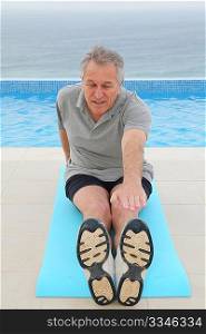 Senior man doing exercises by a swimming-pool