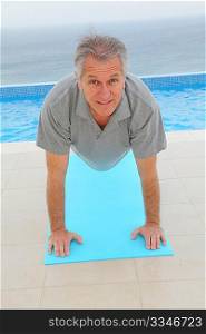 Senior man doing exercises by a swimming-pool