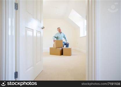 Senior Man Downsizing In Retirement Sitting On Boxes In New Home On Moving Day