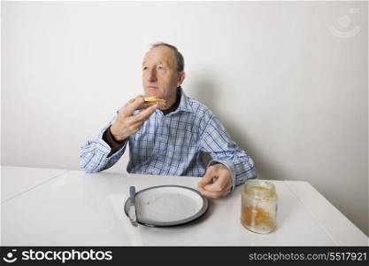 Senior man eating bread spread with sweet jelly jam at table