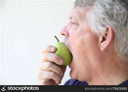 Senior man eats a fresh pear.