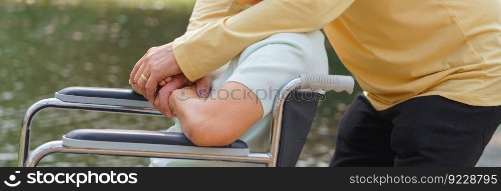 Senior man embracing disabled wife in wheelchair while relaxation with happiness in the park.