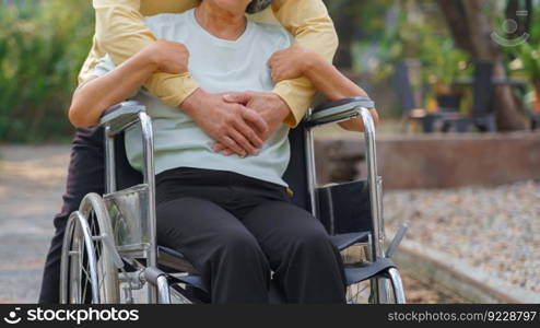 Senior man embracing disabled wife in wheelchair while relaxation with happiness in the park.