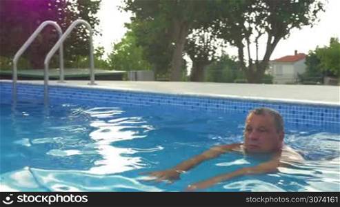 Senior man enjoying swimming in outdoor pool. Relaxing in water on sunny summer day. Recreation and healthy lifestyle