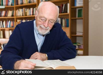 Senior man enjoys a good book in the library. Horizontal view with room for text.