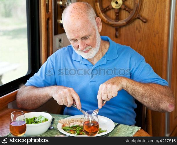 Senior man enjoys a healthy dinner of turkey, green beans and salad, in his motor home.