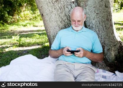 Senior man enjoys texting on his smart phone. Wide view with room for text.