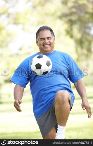 Senior Man Exercising With Football In Park