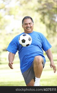 Senior Man Exercising With Football In Park