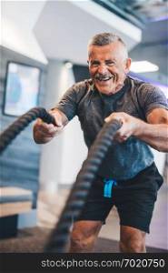 Senior man exercising with ropes at the gym. Physical activity and healthy lifestyle.. Senior man exercising with ropes at the gym.