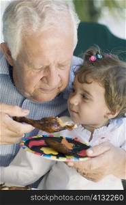 Senior man feeding chicken to his granddaughter