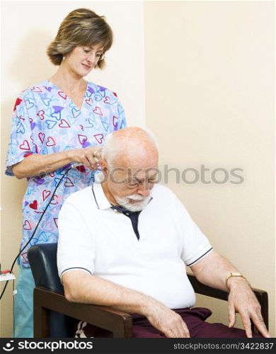 Senior man getting ultrasound therapy on his neck, at the chiropractors office.