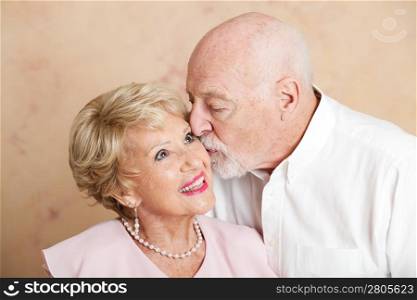 Senior man gives his beautiful wife a kiss on the cheek.