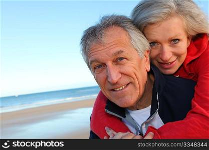 Senior man giving piggyback ride to woman by the sea