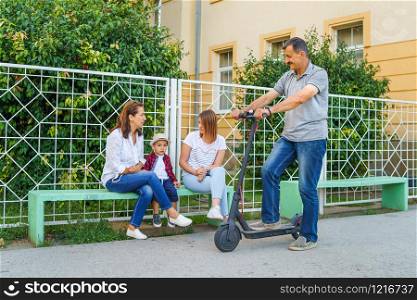 Senior man grandfather riding electric kick scooter while Passing by his family grandson mother small boy outdoor