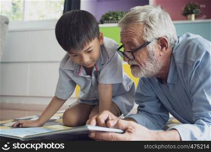 senior man happiness and grandson are sitting on the floor and playing games and reading book at living room together