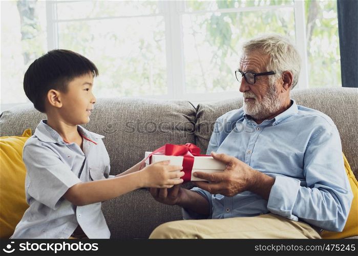 senior man happiness and grandson are sitting on the sofa and give gift at living room together