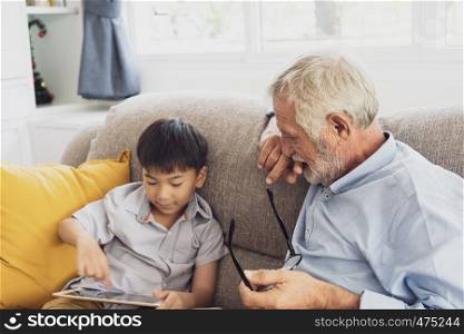 senior man happiness and grandson are sitting on the sofa and playing games and using tablet at living room together