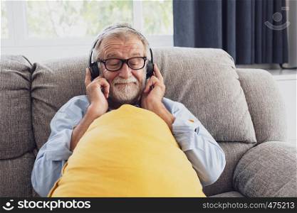 senior man happiness sitting on the sofa and listening music with headphone at living room for relaxing