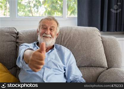senior man happiness sitting on the sofa and smiling and thumbs up or point at living room for relaxing