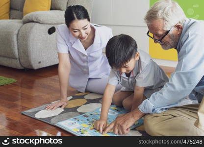 senior man happiness, smiling nurse and grandson are sitting on the floor and playing games at living room together