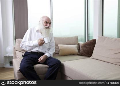 Senior man having coffee while sitting on sofa in apartment