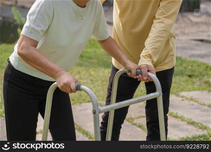 Senior man helping beloved wife walking with walker frame while doing rehab physical in the park.