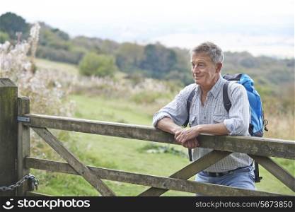 Senior Man Hiking In Countryside Resting By Gate