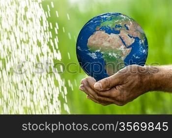 Senior man holding Earth in hands against green spring background. Elements of this image furnished by NASA