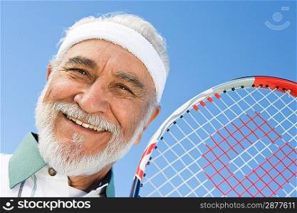Senior man holding tennis racket, portrait
