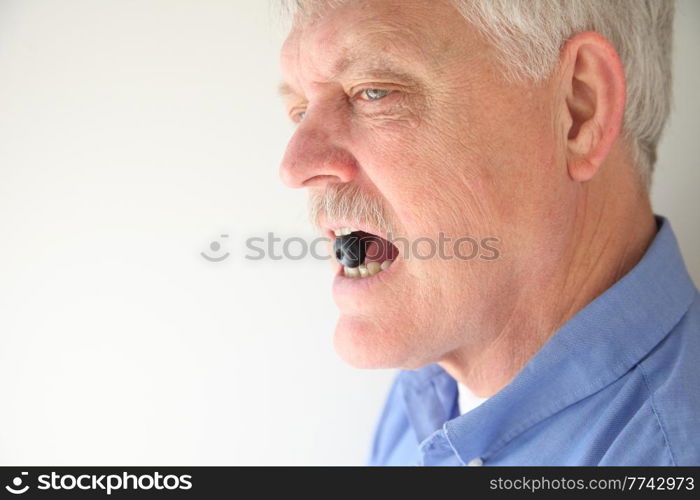 Senior man holds fresh blueberry in his teeth.
