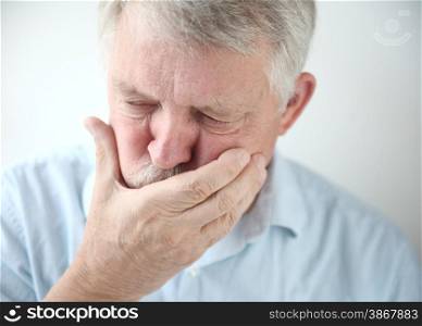 Senior man holds his hand to his mouth while feeling nauseous.