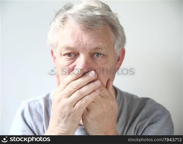 Senior man holds his hands over his mouth.