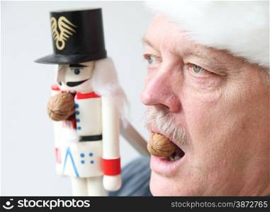Senior man holds walnut in mouth in the manner of a nutcracker.