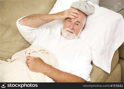 Senior man home sick in bed, with an ice pack on his head. Could be hangover or illness.