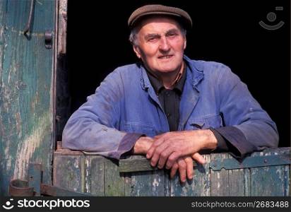 Senior man in cap posing in doorway of wooden barn