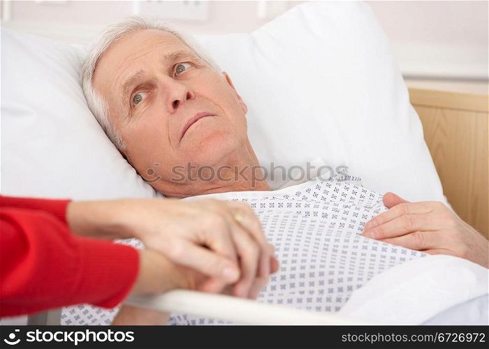 Senior man in hospital bed holding wife&acute;s hand
