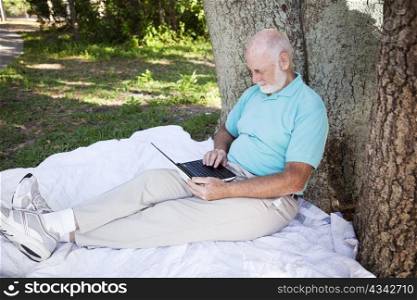 Senior man in the park, working on his netbook computer.