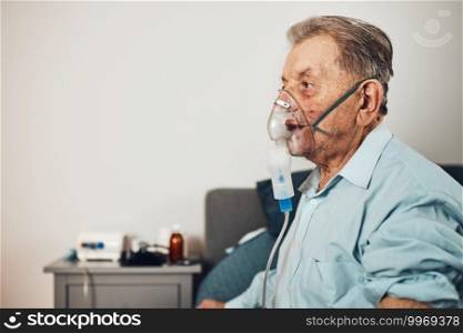 Senior man inhaling airways and lungs applying medicine. Covid-19 or coronavirus treatment. Man breathing through face mask using nebuliser
