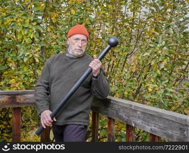 senior man is exercising with a steel mace in his backyard, chilly autumn afternoon