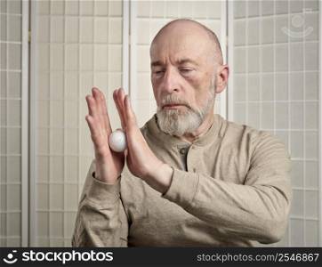 senior man is practicing reflexology therapy by rolling and pressing a golf ball in his hands, self care and massage concept