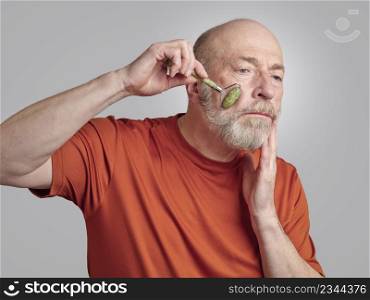 senior man is using a jade stone roller for a face massage, skin care routine concept