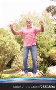 Senior Man Jumping On Trampoline In Garden