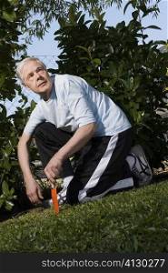 Senior man kneeling in a garden and holding a gardening fork