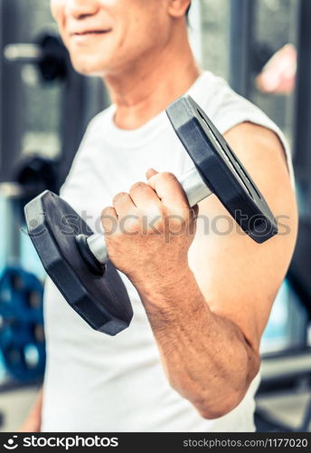 Senior man lifting dumbbell in fitness gym. Senior healthy lifestyle.