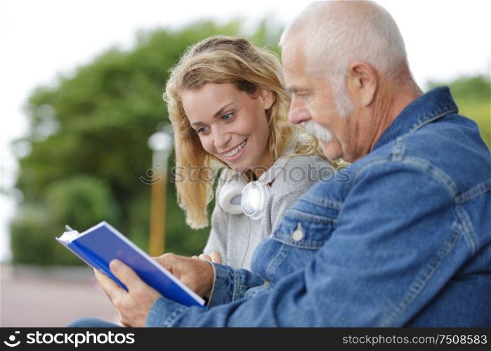 senior man looking at book with young woman