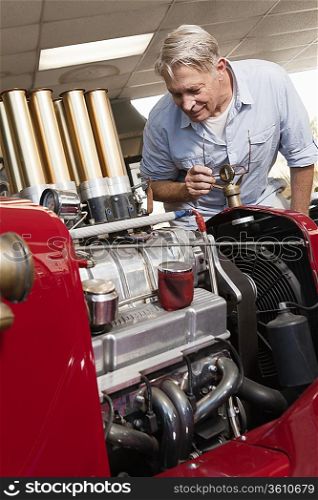 Senior man looking at car engine in automobile repair shop