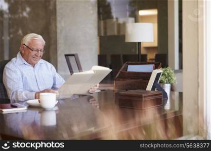 Senior Man Looking At Photo Album Through Window